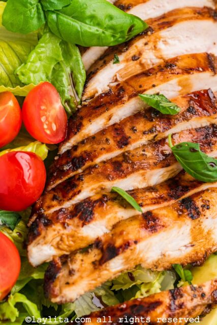Closeup of a sliced grilled chicken breasts on a salad next to cherry tomatoes and basil leaves