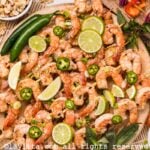 Overhead shot of a platter of grilled shrimp skewers with spicy peppers, veggie skewers, chili flakes and peanut sauce on the side