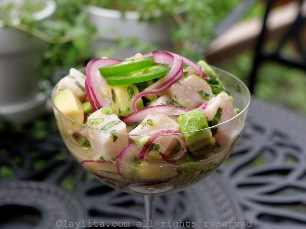 Closeup of hamachi ceviche served in a tall glass on a black garden table with a plant in the background
