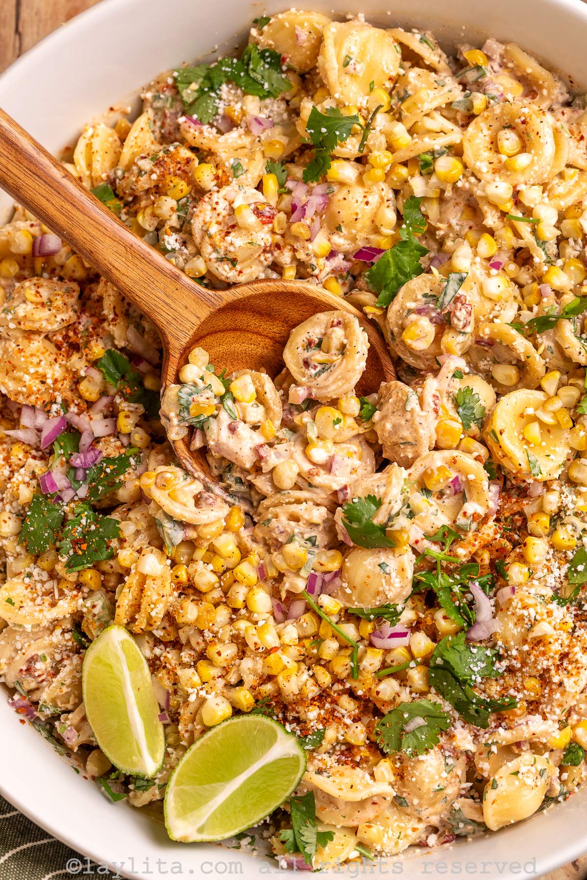 Close up shot of a bowl of Mexican corn pasta salad with a wooden spoon in the bowl