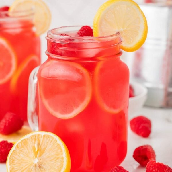 Side view of a jar of raspberry lemonade, garnished with lemons and a straw.