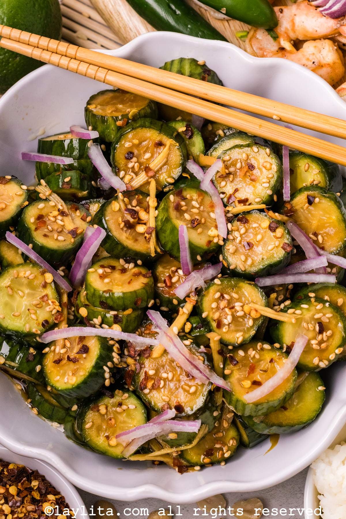 Overhead view of a white bowl of Asian cucumber salad with red onion slices, there is a set of chopsticks resting on the side of the bowl