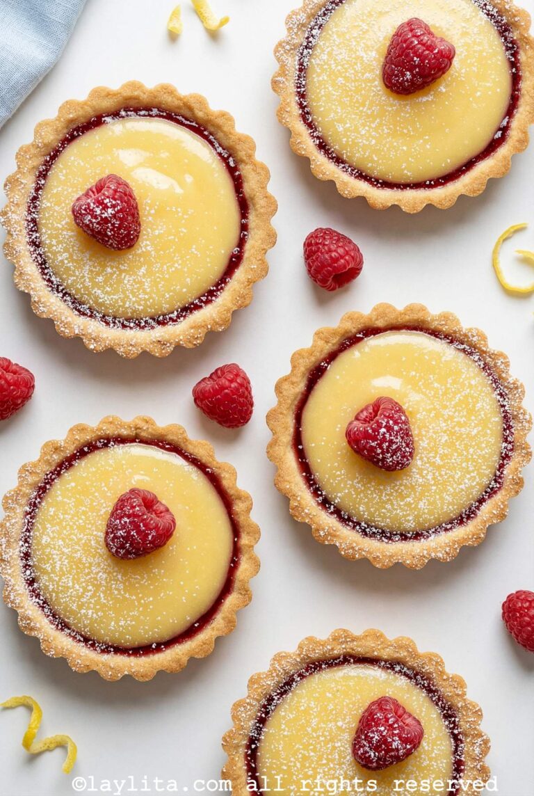 Overhead shot of five raspberry lemon tartlets all with one raspberry on top and some powdered sugar