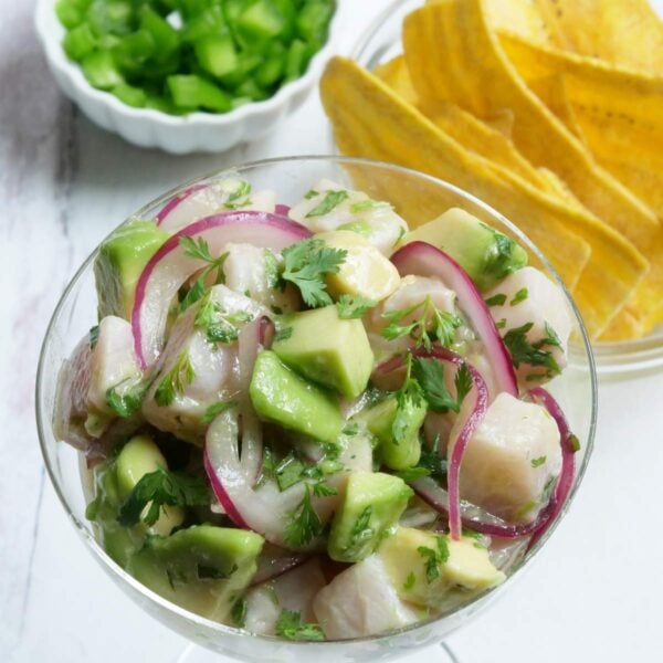 Overhead shot of hamachi ceviche served in a glass with a bowl of plantain chips and chopped jalapeños in the background
