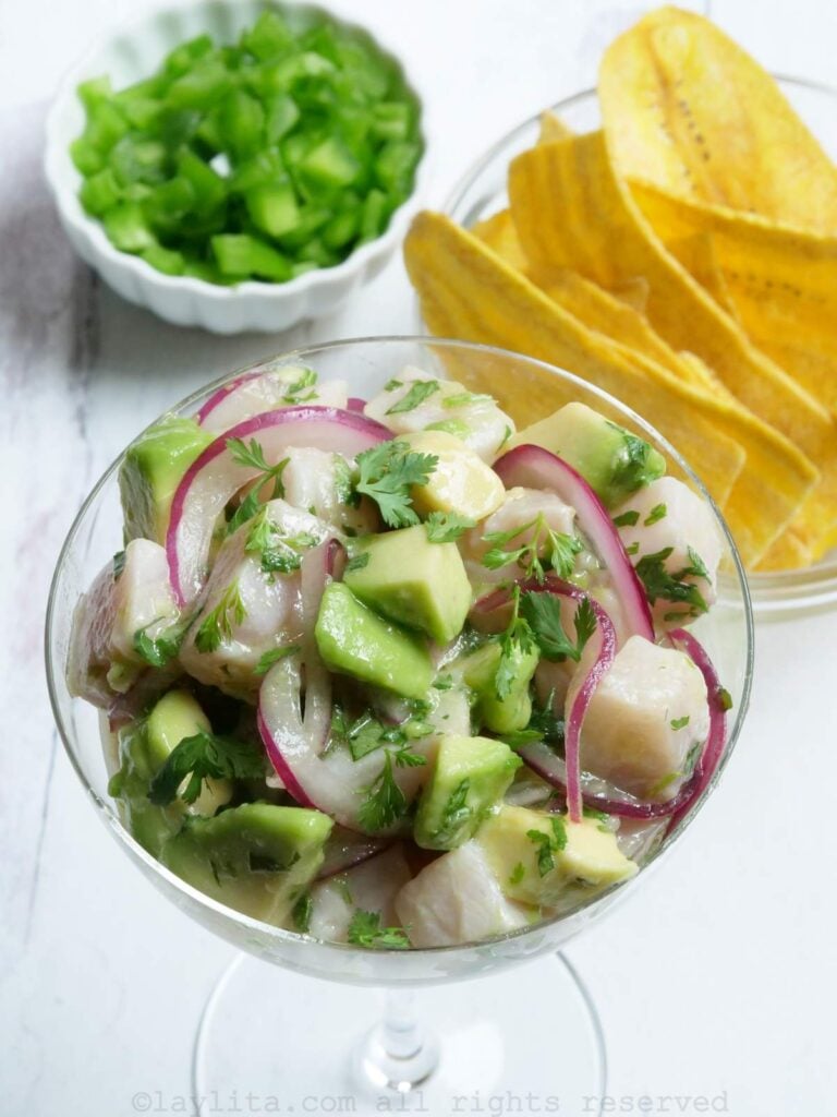 Overhead shot of hamachi ceviche served in a glass with a bowl of plantain chips and chopped jalapeños in the background