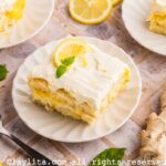 Side view of three plates with portions of lemon tiramisu on a tile counter, with a spoon, lemon slices, mint leaves and ginger on the side
