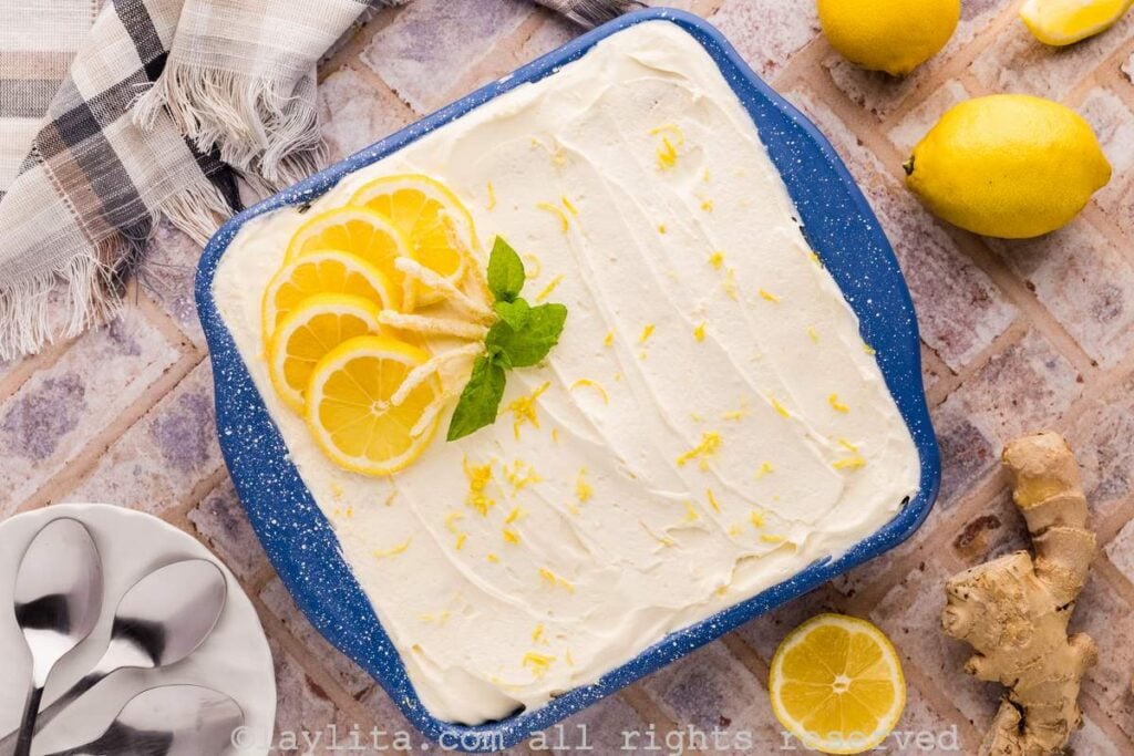 Overhead shot of a square blue baking mold filled with lemon tiramisu, garnished with lemon zest, lemon slices and mint leaves