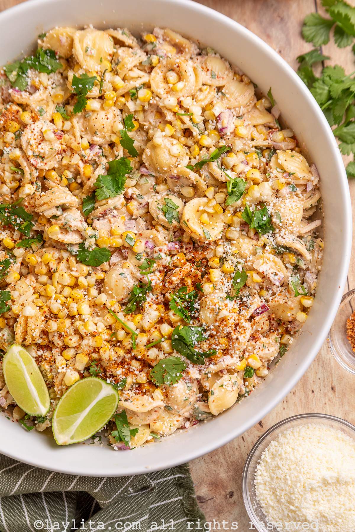 Overhead partial view of a white bowl with corn pasta salad, with a small bowl of cotija cheese on the side