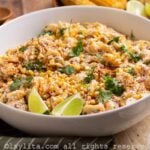 A white bowl filled with corn pasta salad garnished with lime wedges and chopped cilantro leaves