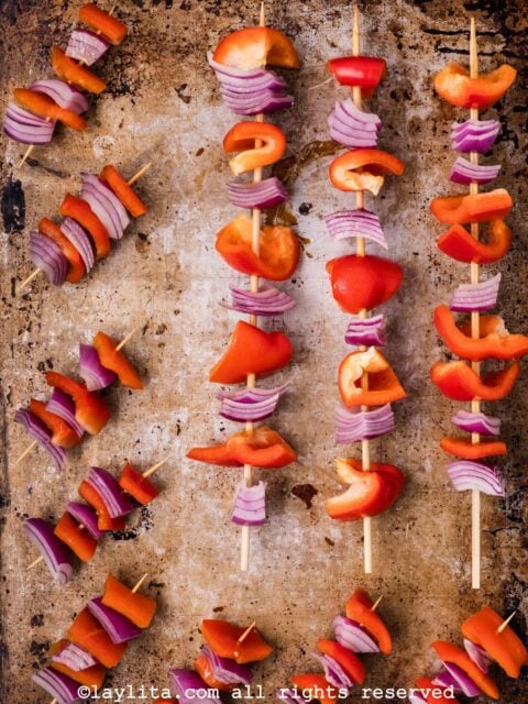 Skewers of red bell pepper and red onion on a baking sheet