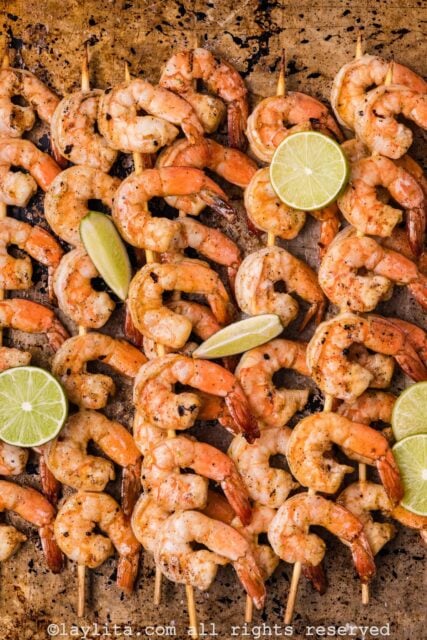 A baking sheet with several grilled shrimp skewers and lime wedges
