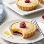 Raspberry lemon tart on a plate with a bite missing, with more tarts in the background.
