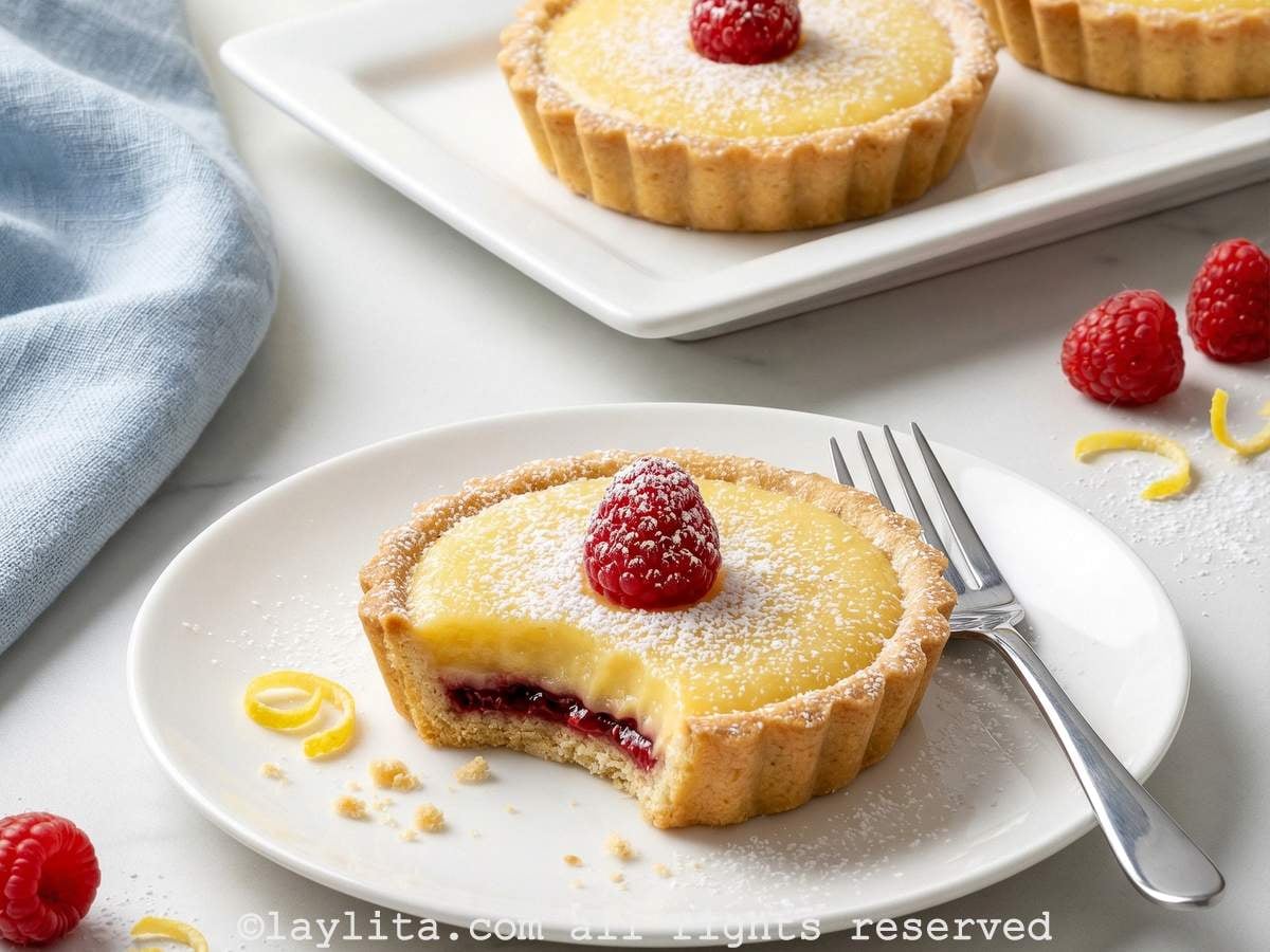 Raspberry lemon tart on a plate with a bite missing, with more tarts in the background.