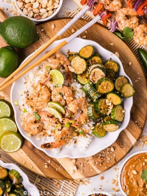 Overhead view of a plate of rice with shrimp and peanut sauce on top, next to some cucumber salad