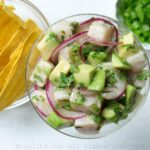 Hamachi ceviche in a glass with a bowl of plantain chifles and jalapeños next to it.
