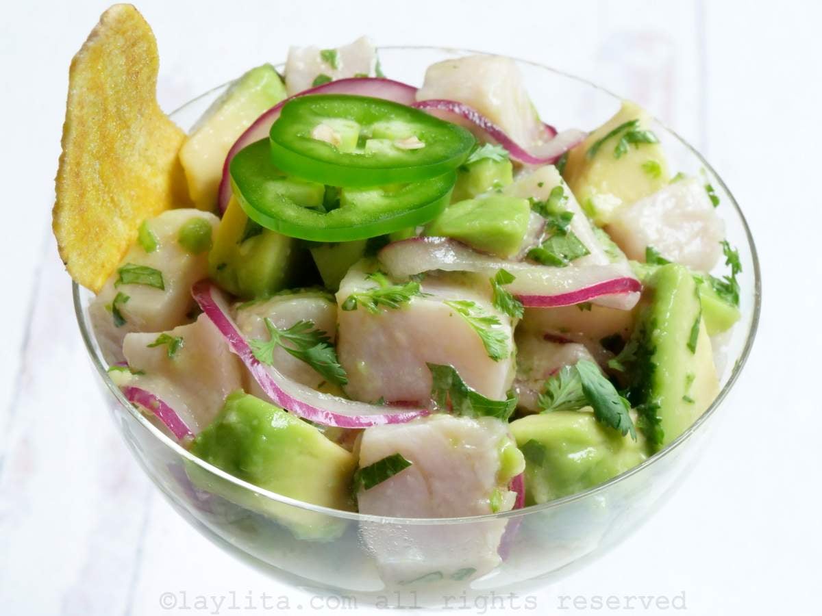 Hamachi ceviche served in a tall glass garnished with jalapeño slices and a couple of plantain chifle chips on the side.