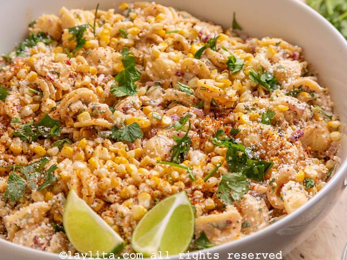 Smoky Chipotle Street Corn Pasta Salad in a white bowl garnished with lime slices and chopped cilantro