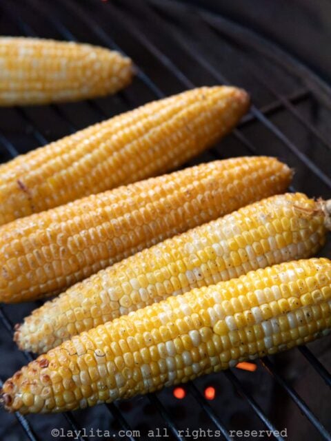 Sideview of five ears of corn cooking on a grill