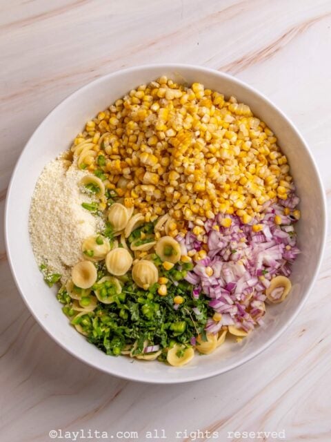 Grilled corn kernels, cooked pasta, onions, cilantro and cotija cheese in a bowl