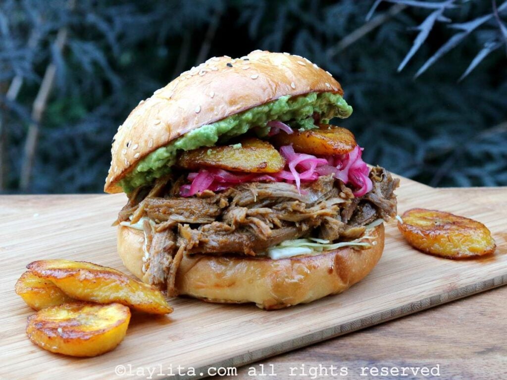 Chicha pulled pork served in a sandwich with toppings and fried plantains on the side