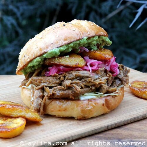 Chicha pulled pork served in a sandwich with toppings and fried plantains on the side