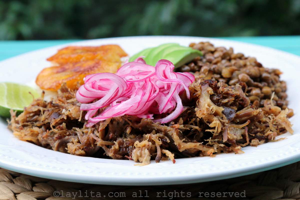 Side view of chicha pulled pork on a plate with sides, topped with red onions.