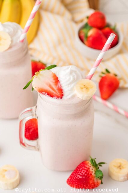 Strawberry banana milkshake in a mason jar glass topped with a fresh strawberry and banana slice and whipped cream.
