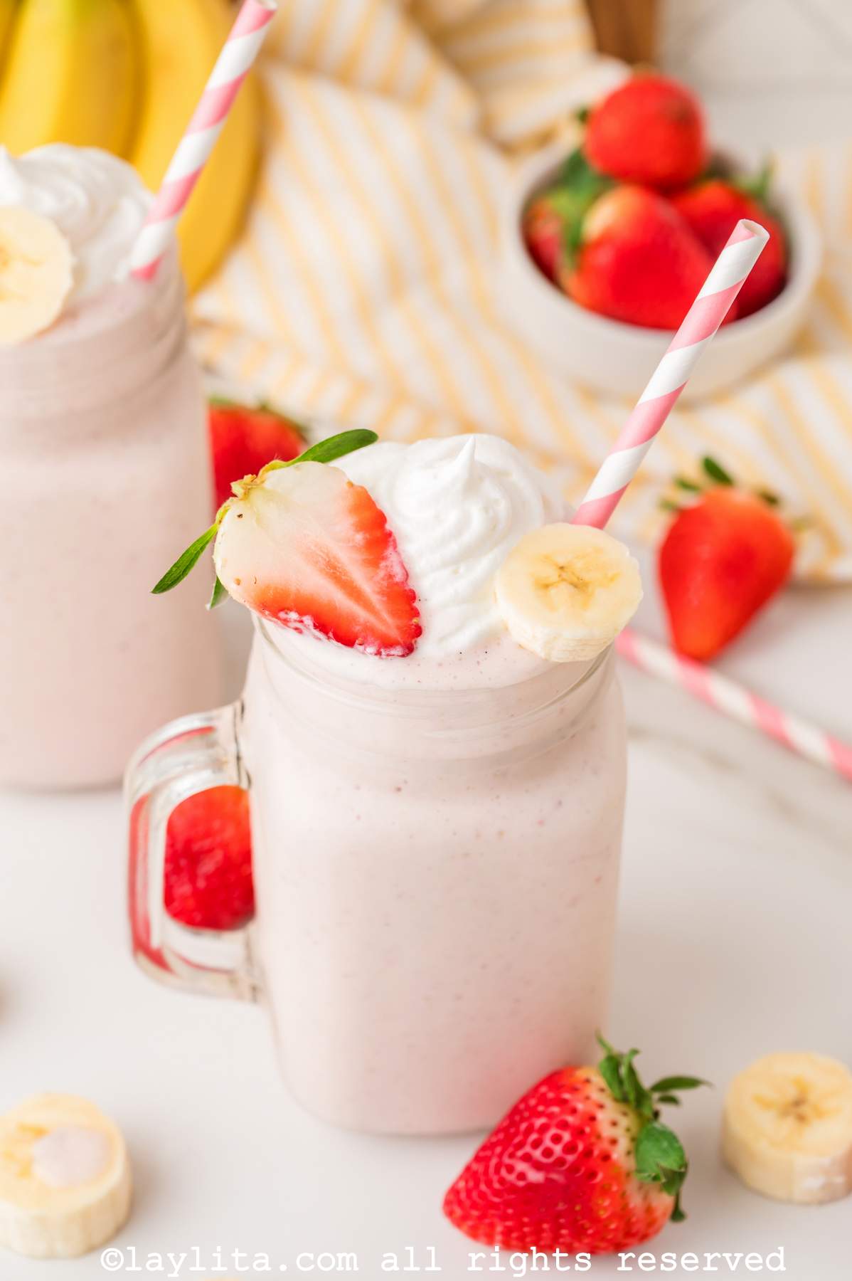 Strawberry banana milkshake in a mason jar glass topped with a fresh strawberry and banana slice and whipped cream.