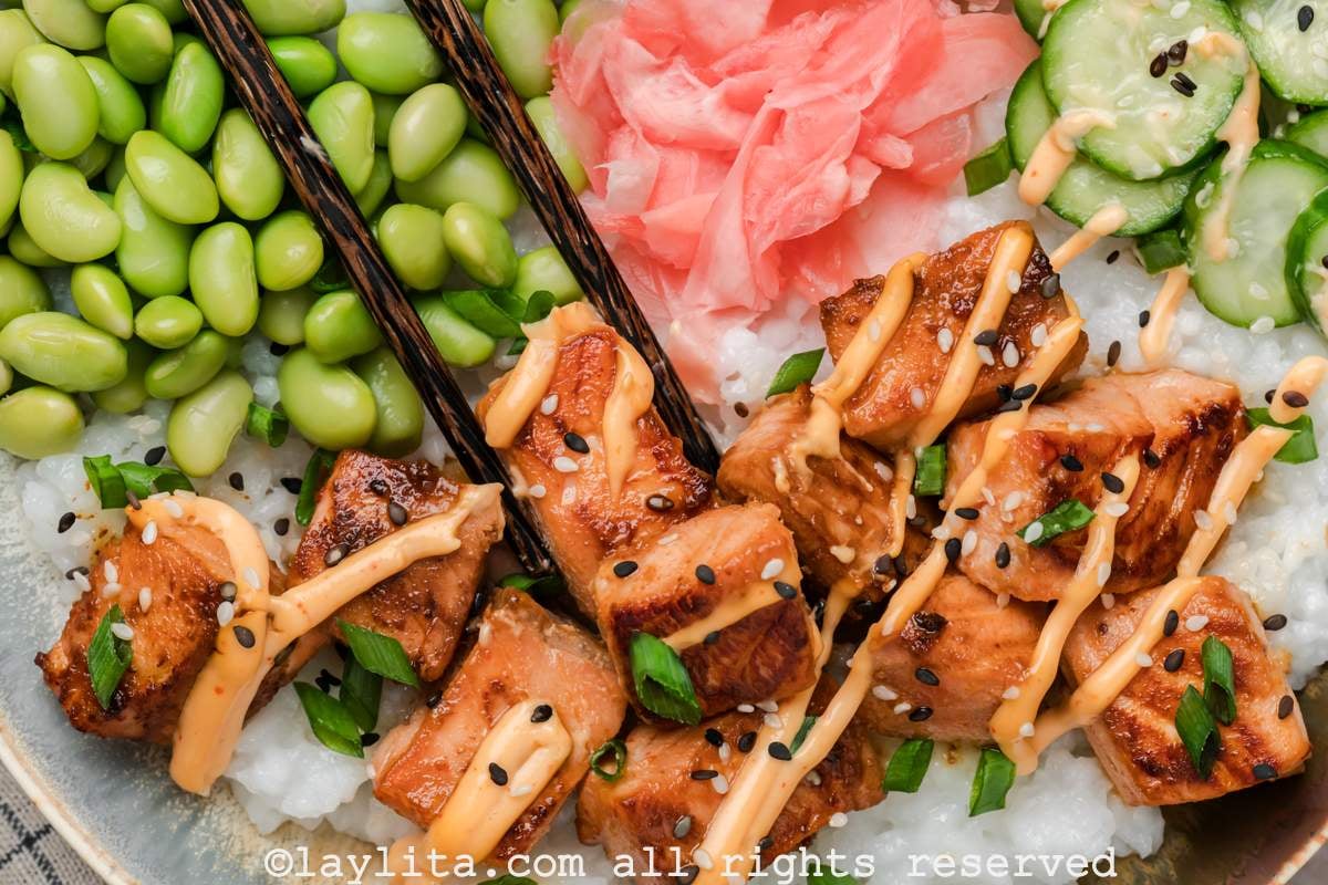 Chopsticks picking up a piece of crispy salmon from a bowl.