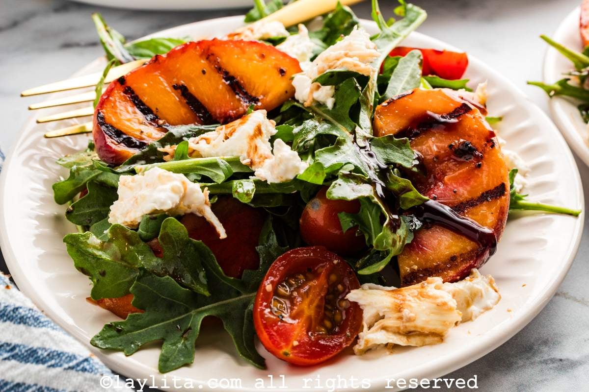 Side view of a grilled peach burrata salad with arugula on a white plate