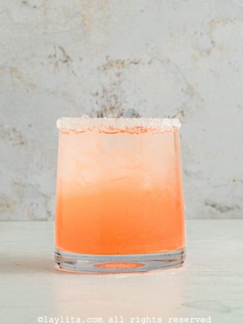 A glass filled with a grapefruit tequila cocktail topped with sparkling water on a kitchen counter
