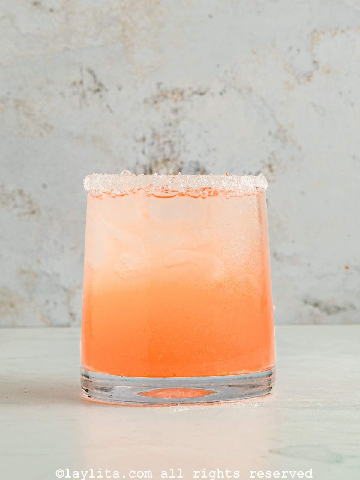 A glass filled with a grapefruit tequila cocktail topped with sparkling water on a kitchen counter