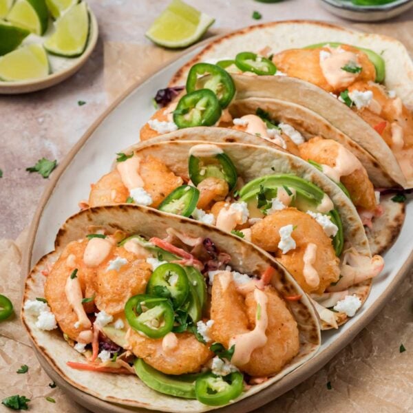 Sideview of a platter of baja shrimp tacos surrounded by limes and fresh jalapenos.