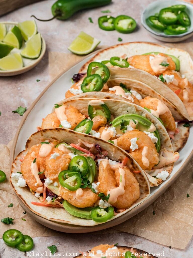 Sideview of a platter of baja shrimp tacos surrounded by limes and fresh jalapenos.