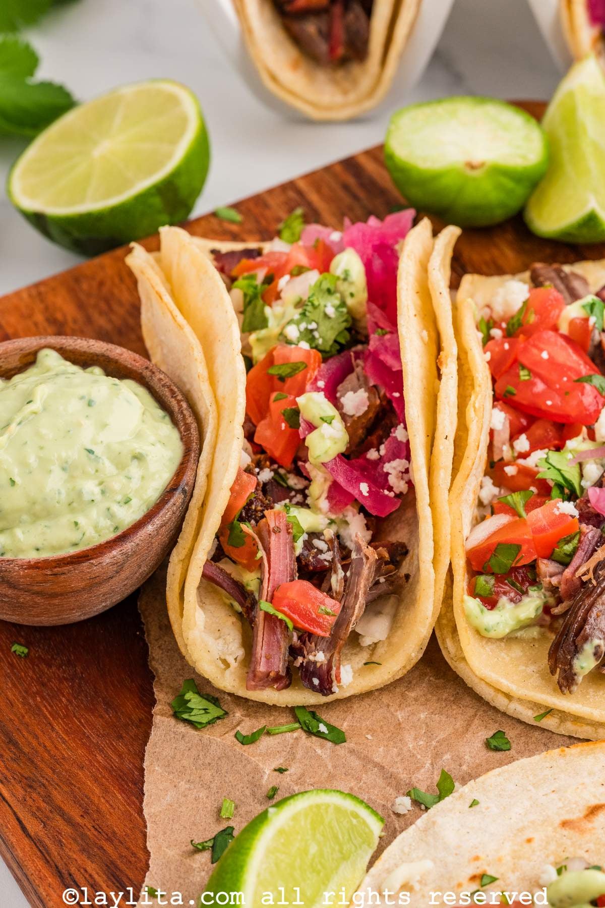 Two beef brisket tacos leaning on each other next to a small bowl of sauce.