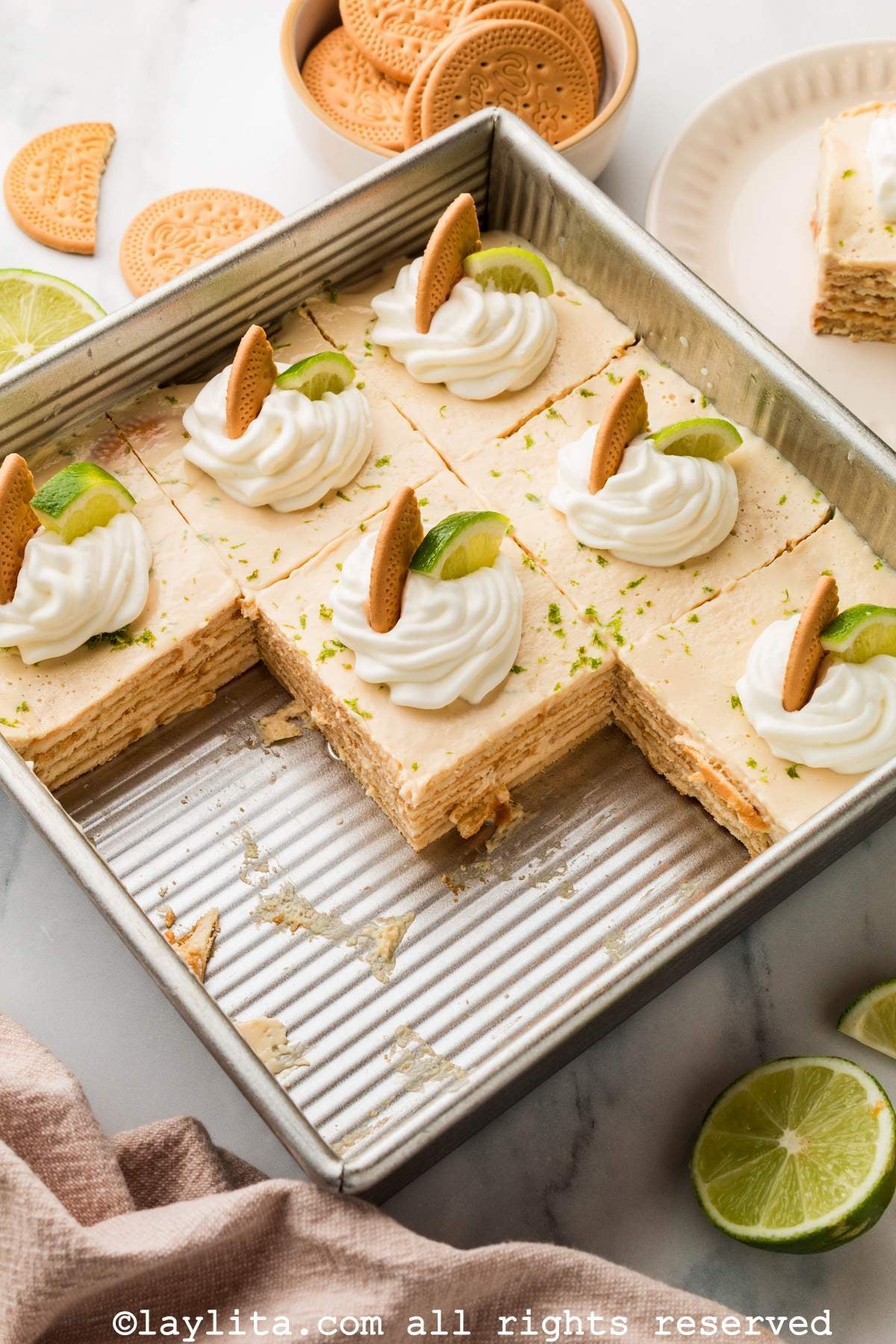 Carlota de limón in a baking dish with each slice decorated with whipped cream and cookies.