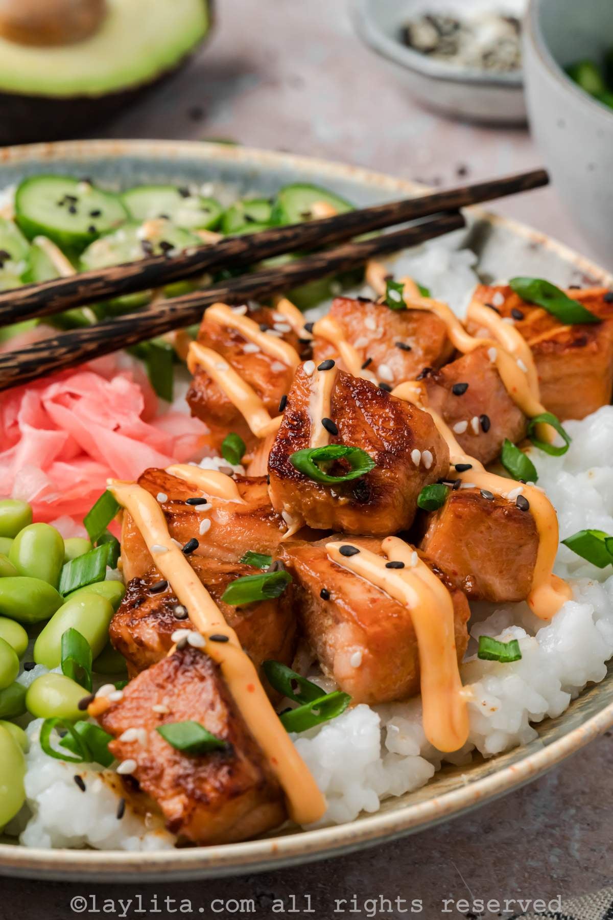 Close up of crispy salmon bites with mayo drizzle on top in a bowl with rice and vegetables.