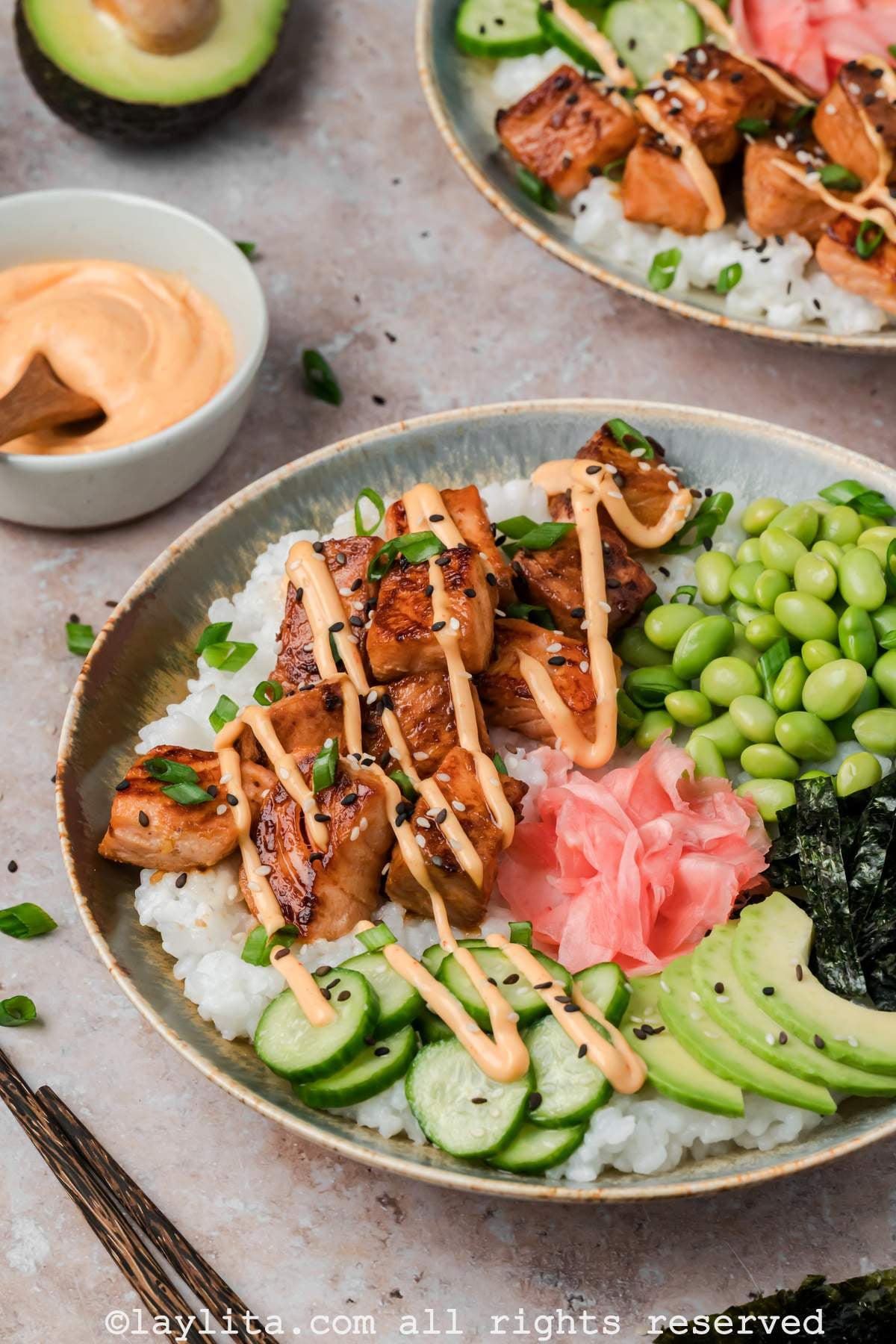 Side view of two crispy salmon bites sushi bowls with salmon bites, vegetables, and spicy mayo drizzled on top.