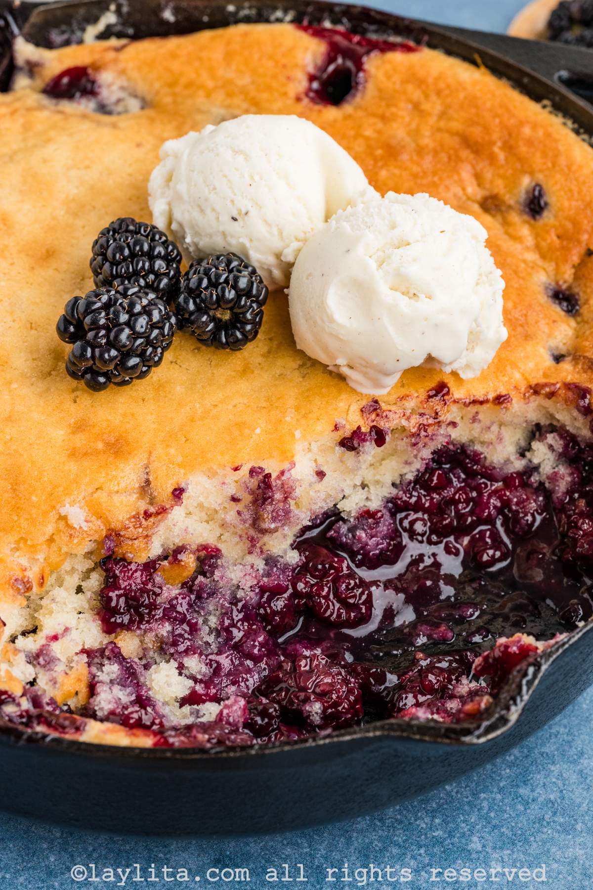 Blackberry cobbler in a cast iron skillet with two scoops of ice cream on top