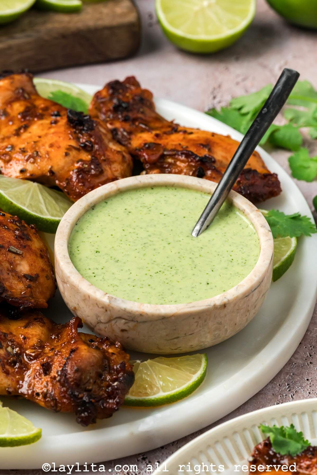 A bowl of Peruvian Ají Verde Green Sauce on plate next to several roasted chicken thighs