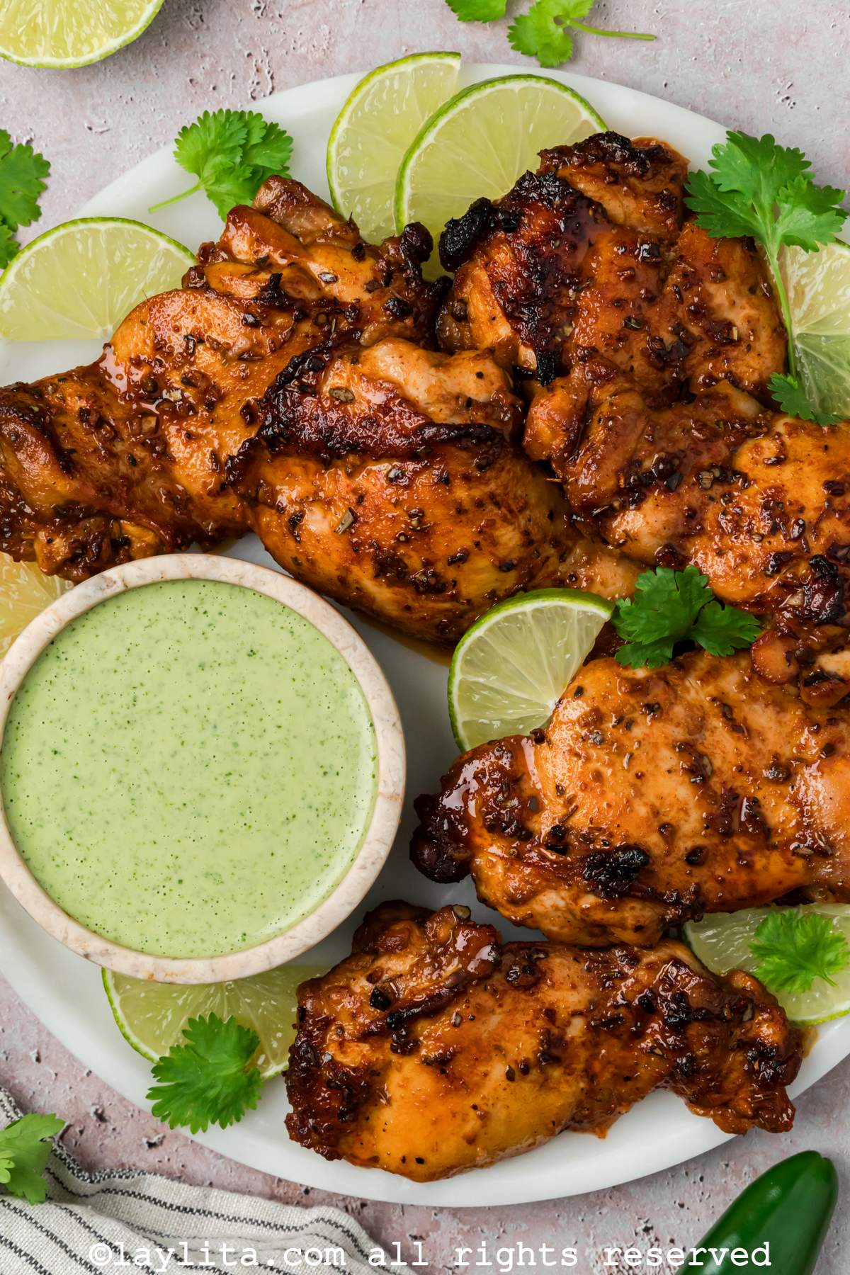 Overhead closeup shot of Peruvian chicken thighs on a plate next to a small bowl of green sauce.