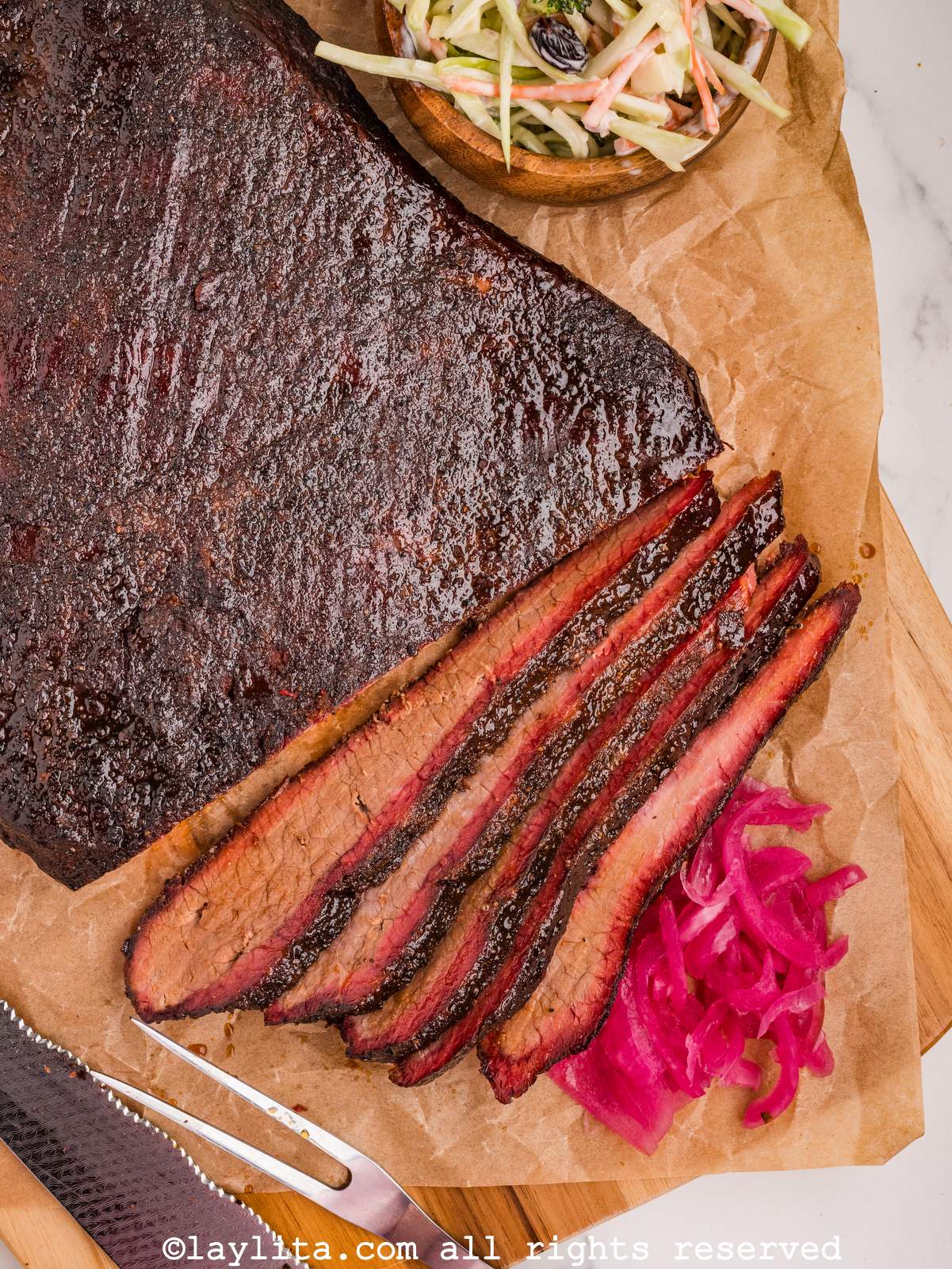 Overhead closeup shot of brisket with some slices off the end next to pickled onions and pickles.
