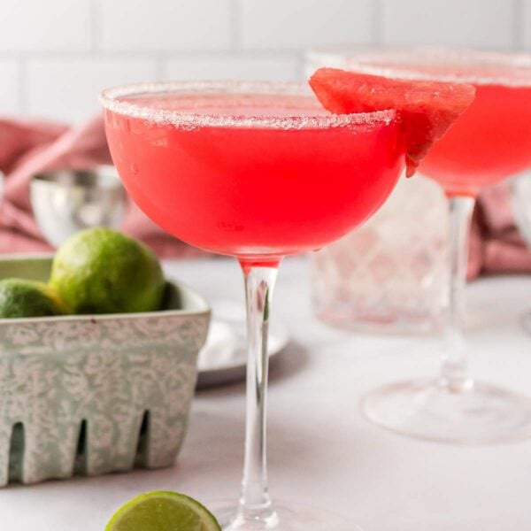 Two watermelon margaritas in coupe glasses, both garnished with sugar and watermelon.