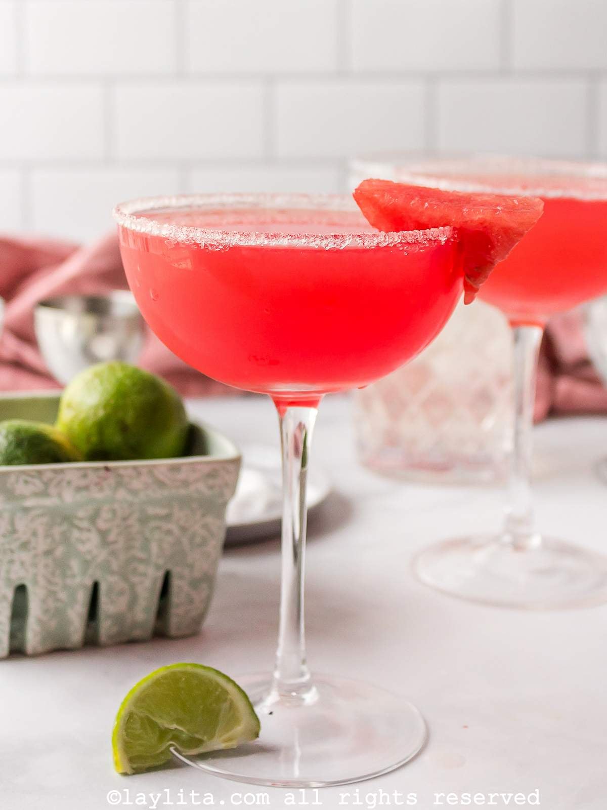 Two watermelon margaritas in coupe glasses, both garnished with sugar and watermelon.