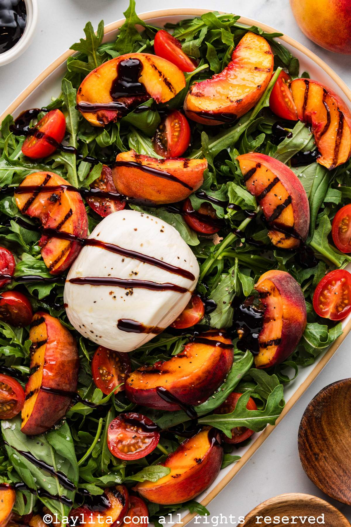 Overhead view of a platter of peach burrata salad drizzled with balsamic glaze