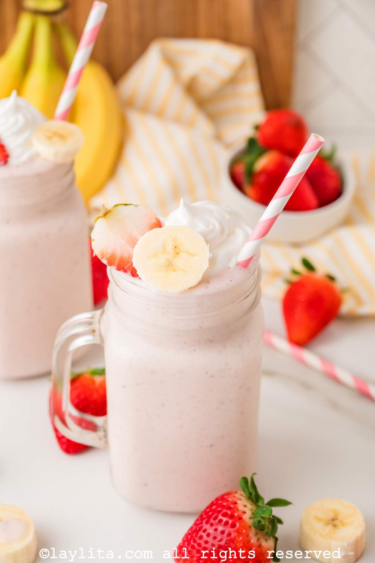 Strawberry banana smoothie in a glass jar topped with a fresh strawberry and banana slice and whipped cream.