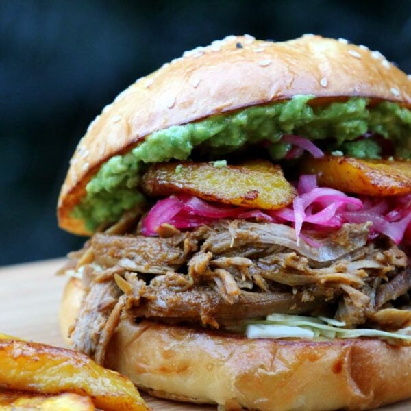 Side view of chicha pulled pork sandwich with toppings and fried plantains