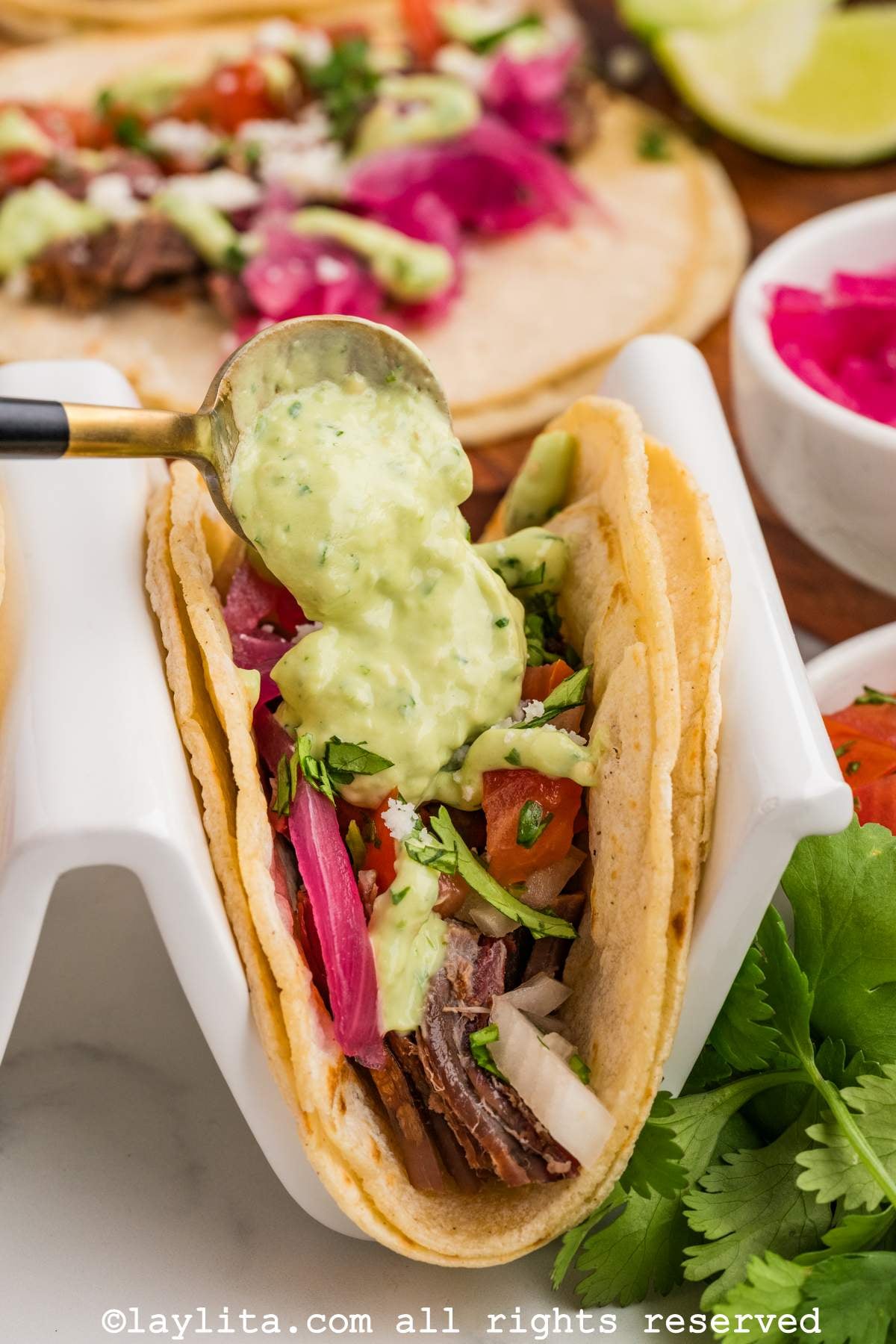 Spoon scooping some green sauce over the top of a beef brisket taco.
