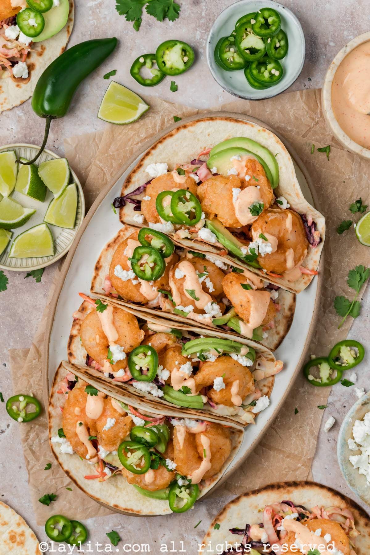 Overhead view of a serving platter of four baja shrimp tacos, all drizzled with baja sauce on top