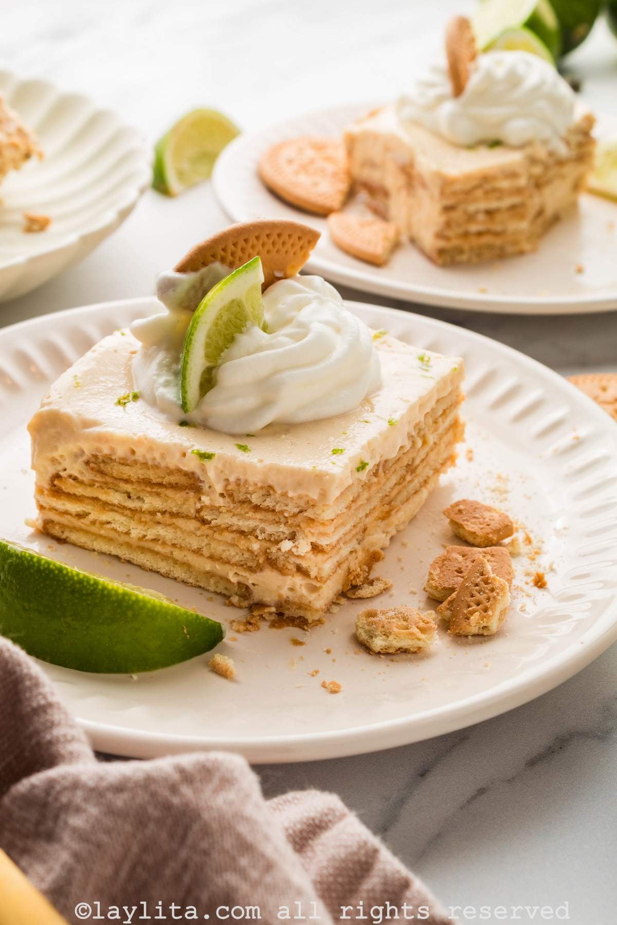 A slice of carlota de limón on a white plate with some cookies and a lime wedge on the plate.